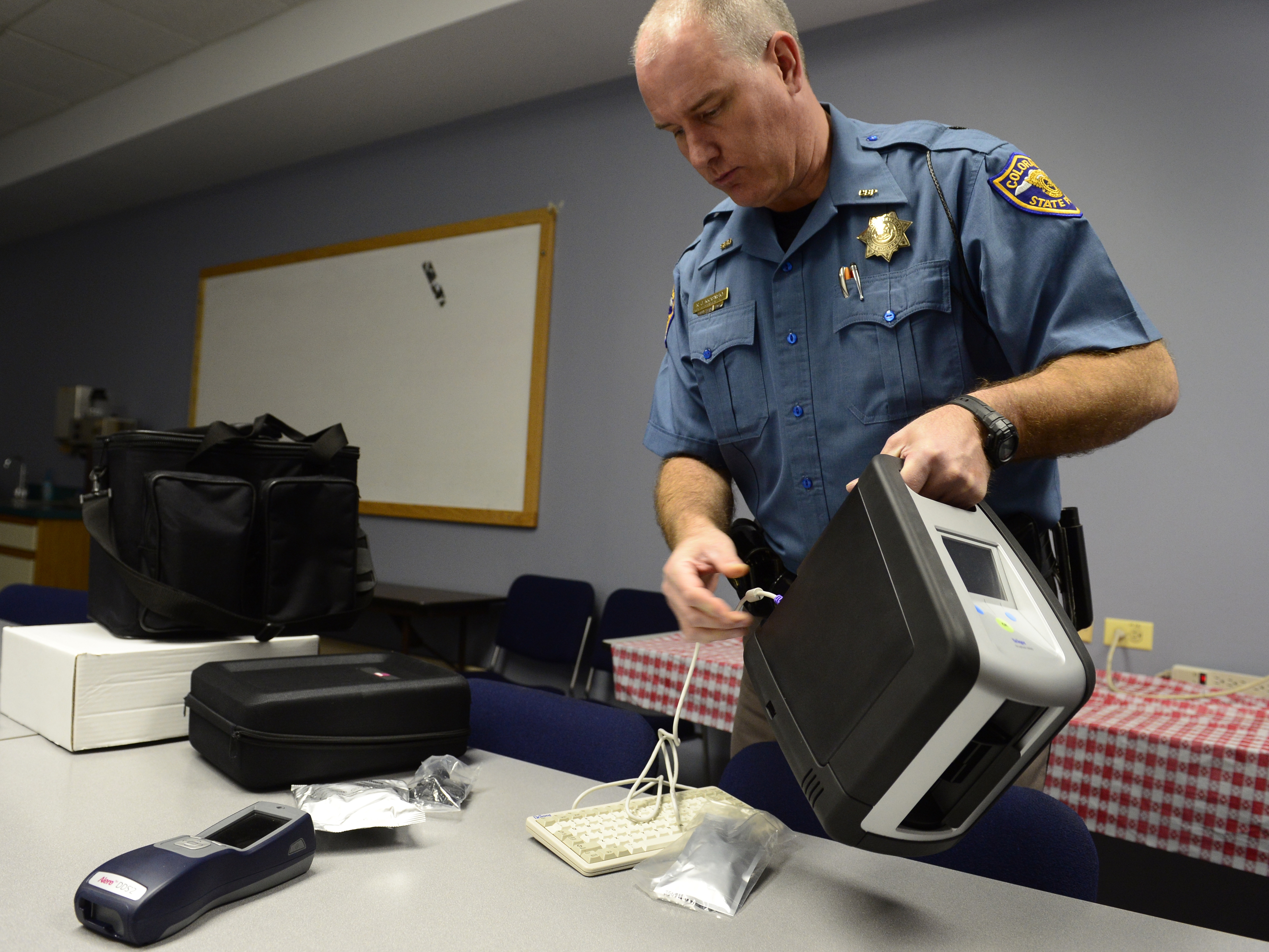 caption: Colorado State Trooper Ron Krasnisky shows the department's oral fluid drug screen testing device, used during a pilot program that ended earlier this year. The system uses a saliva collection device to test impaired drivers for marijuana use as well as other drugs.