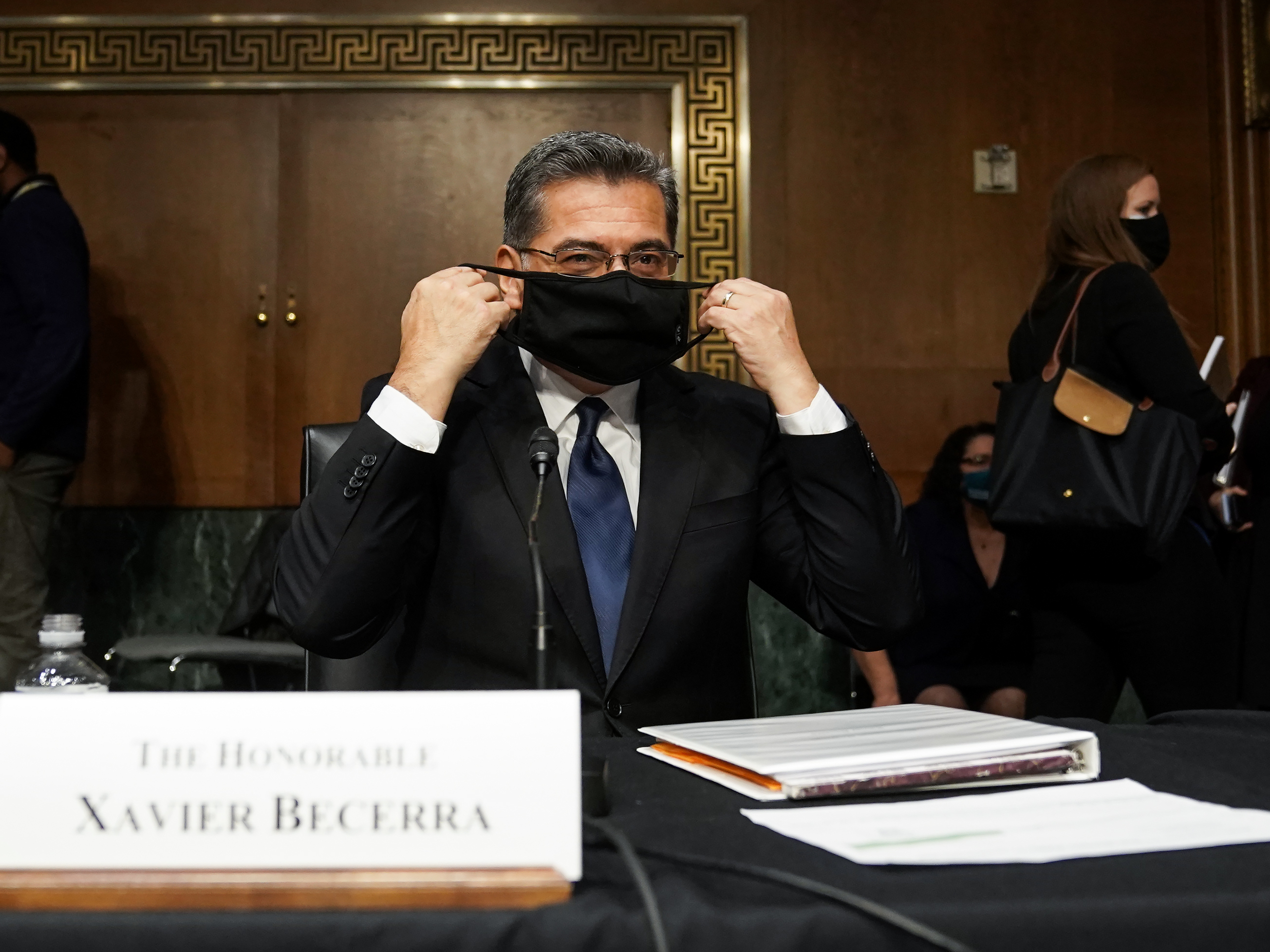 caption: Xavier Becerra, then nominee for secretary of Health and Human Services, puts on his protective mask at his Senate Finance Committee confirmation hearing in February.