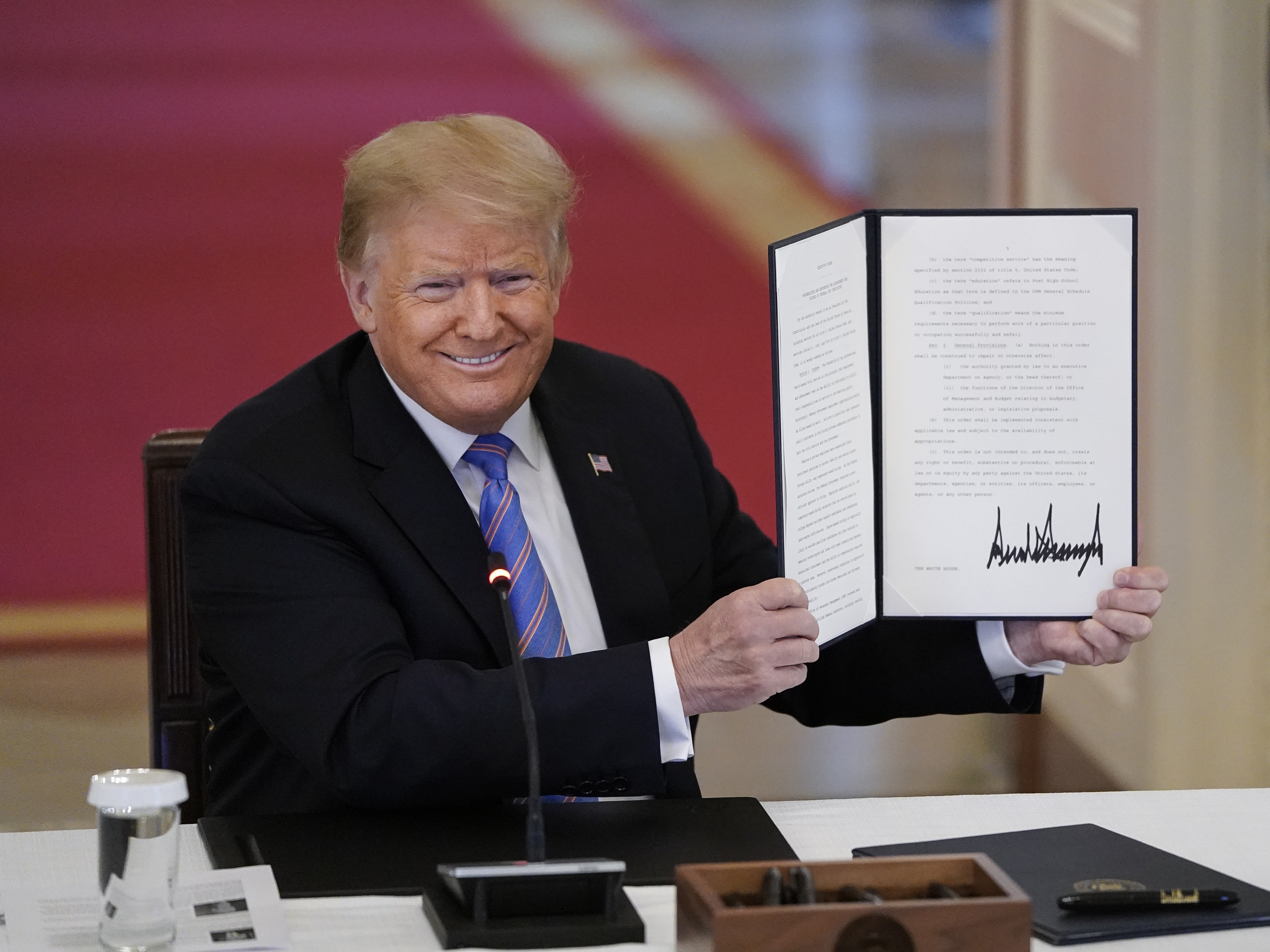caption: Then-President Donald Trump signs an executive order related to reforming the hiring process for federal jobs on June 26, 2020.