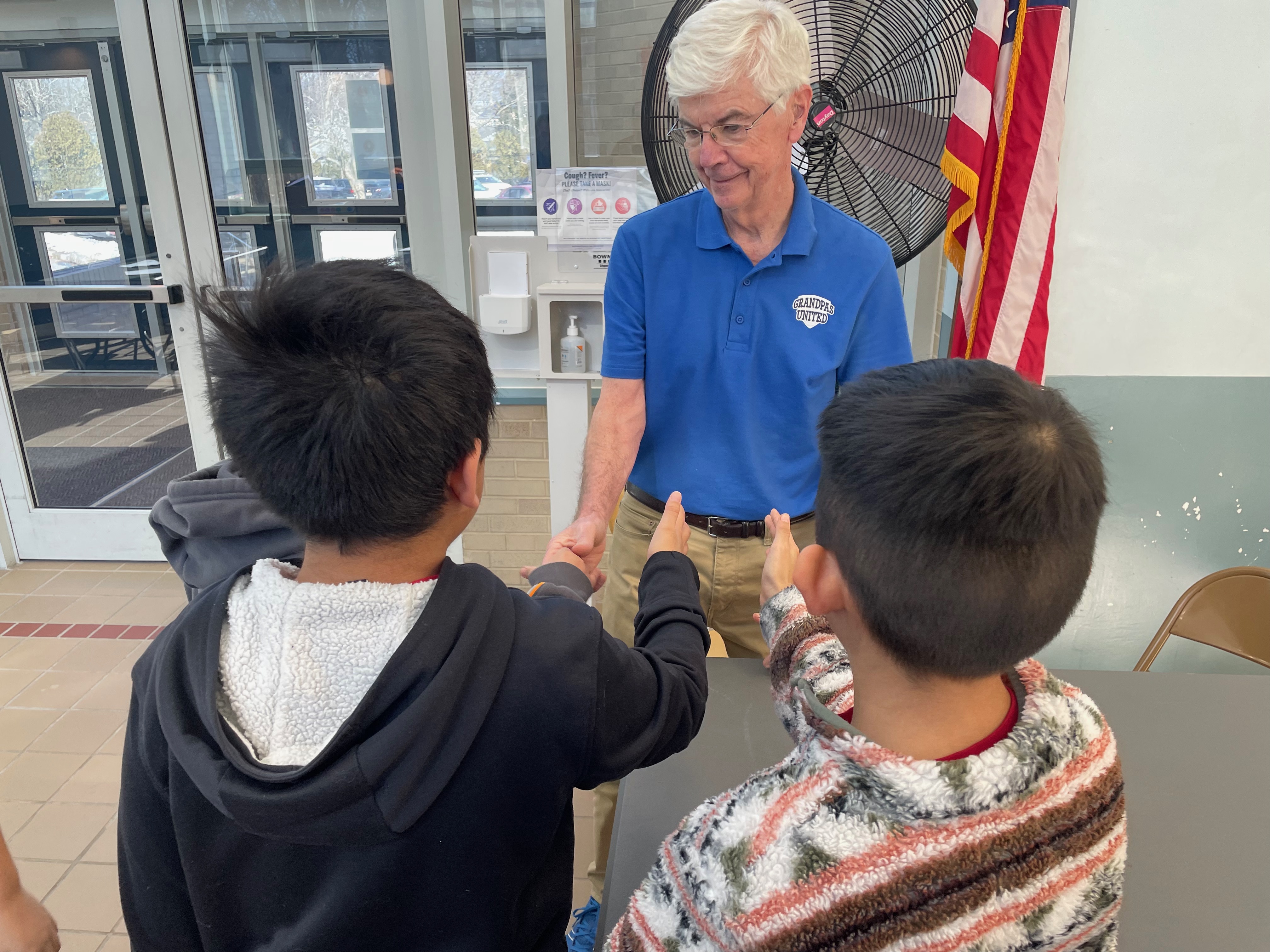 caption: Fourth-graders line up to shake hands with Dennis Cuddy, one of the volunteers with Grandpas United, in White Plains, N.Y.