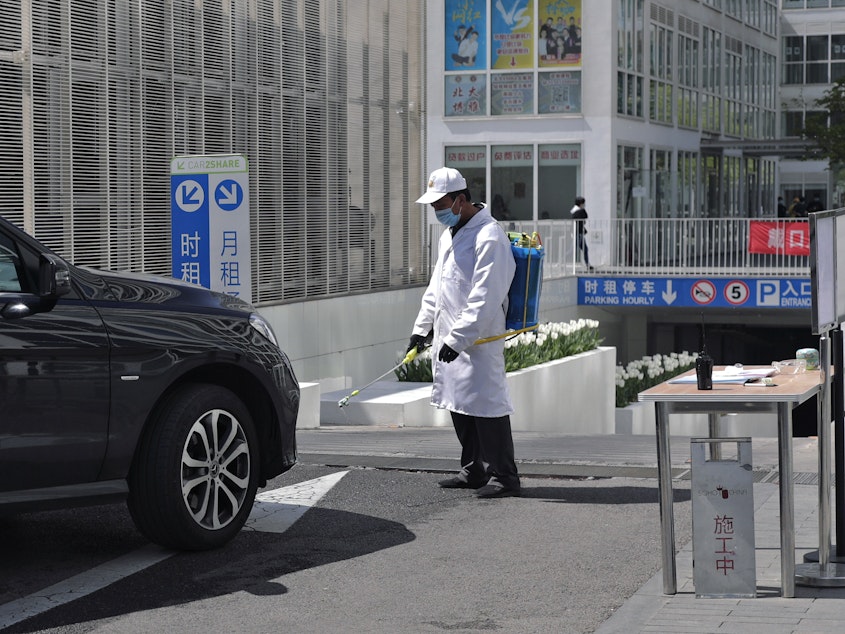 caption: A worker wearing a protective face mask to prevent the spread of the new coronavirus sprays disinfectant as a vehicle prepares to enter an office building carpark in Beijing, on Monday.