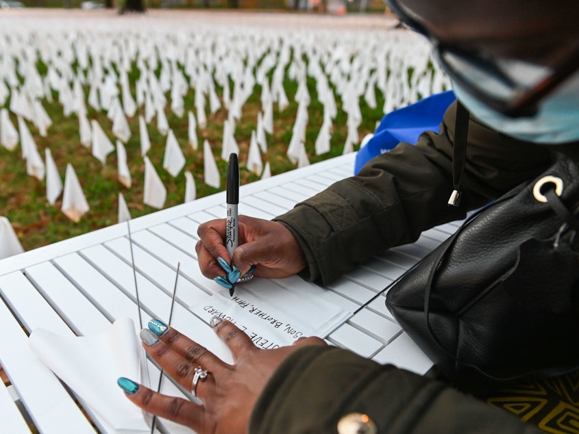 caption: Patrice Howard writes on white flags before planting them to remember her recently deceased father and close friends in November at "IN AMERICA How Could This Happen...," a public art installation in Washington, D.C. Led by artist Suzanne Firstenberg, volunteers planted white flags in a field to symbolize each life lost to COVID-19 in the U.S.