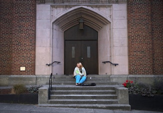 caption: Milee Ballweg sleeps on the steps of a church in Seattle's University District. She's 20, her hair is blonde tinged with pink, and she wears ripped jeans and a PokÃ©mon T-shirt. She sleeps wrapped in gray packing blankets that cover her face. 