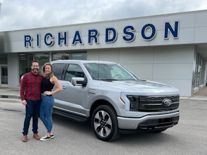 caption: Nick Schmidt poses with his wife after picking up his brand new electric F-150. Schmidt was the first buyer to get the F-150 Lightning as auto makers are betting billions in an electric future.