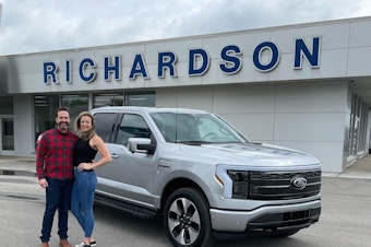 caption: Nick Schmidt poses with his wife after picking up his brand new electric F-150. Schmidt was the first buyer to get the F-150 Lightning as auto makers are betting billions in an electric future.