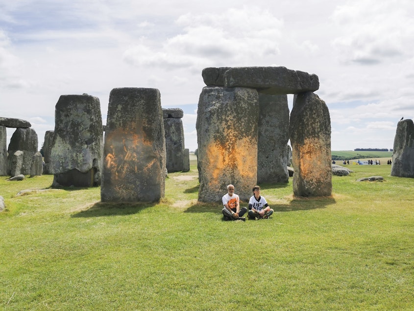 caption: In this handout photo, Just Stop Oil protesters sit after spraying an orange substance on Stonehenge, in Salisbury, England, on Wednesday. (Just Stop Oil via AP)