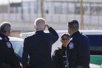 caption: President Biden looks toward a large "Welcome to Mexico" sign that is hung over the Bridge of the Americas as he tours the port of entry in El Paso Texas on Jan. 8.