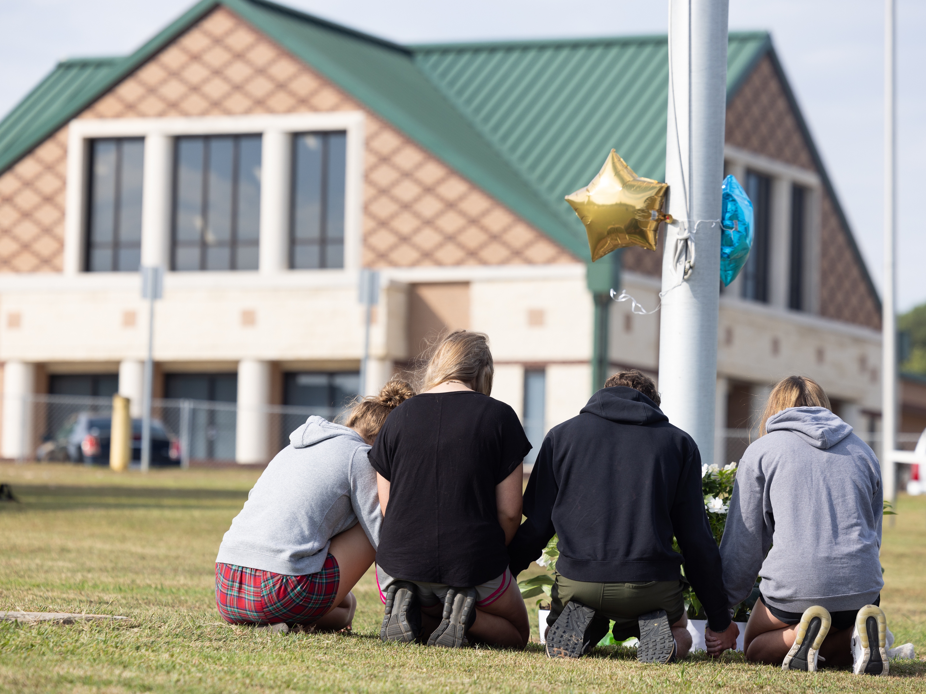 caption: Students kneel in front of a makeshift memorial in front of Apalachee High School on in Winder, Ga., on Thursday, one day after two students and two teachers were shot and killed at the school.