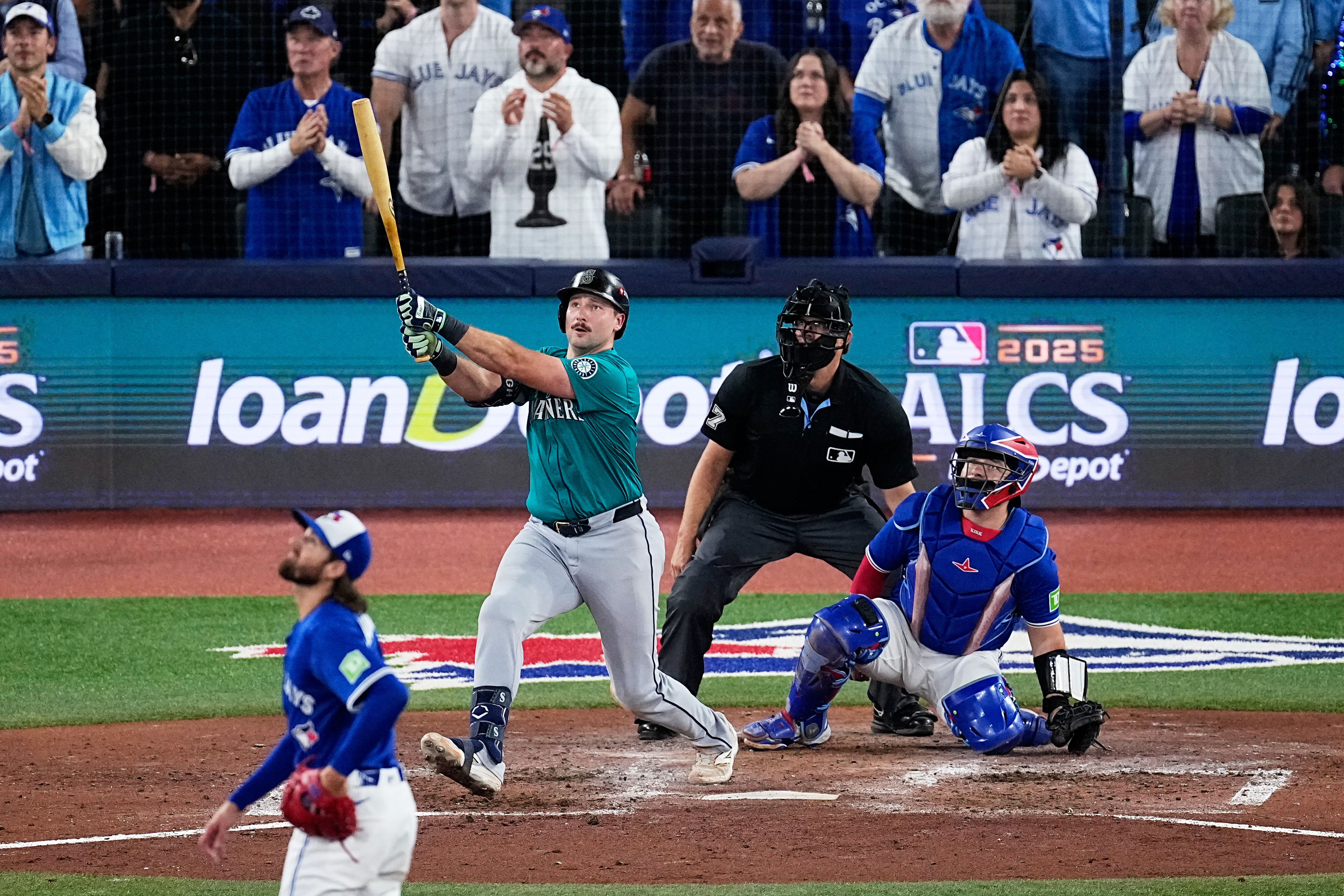 caption: Seattle Mariners' Cal Raleigh watches his solo home run take flight as Toronto Blue Jays pitcher Kevin Gausman, left, and Alejandro Kirk, right, look on during the sixth inning in Game 1 of baseball's American League Championship Series, Sunday, Oct. 12, 2025, in Toronto. 
