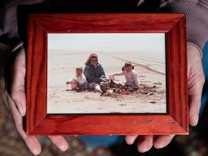 caption: Simone Elliot holds a childhood photo of she and her sister with their mother.