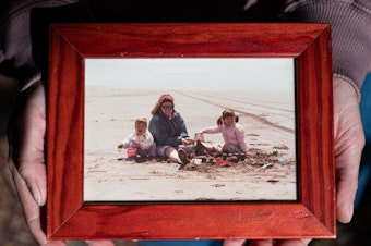 caption: Simone Elliot holds a childhood photo of she and her sister with their mother.