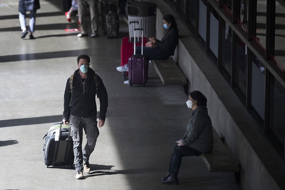 caption: Masked travelers exit Seattle-Tacoma International Airport on Monday, May 18, 2020, in Seattle. All passengers and employees traveling through the airport are required to wear face coverings beginning today, Monday, May 18. 