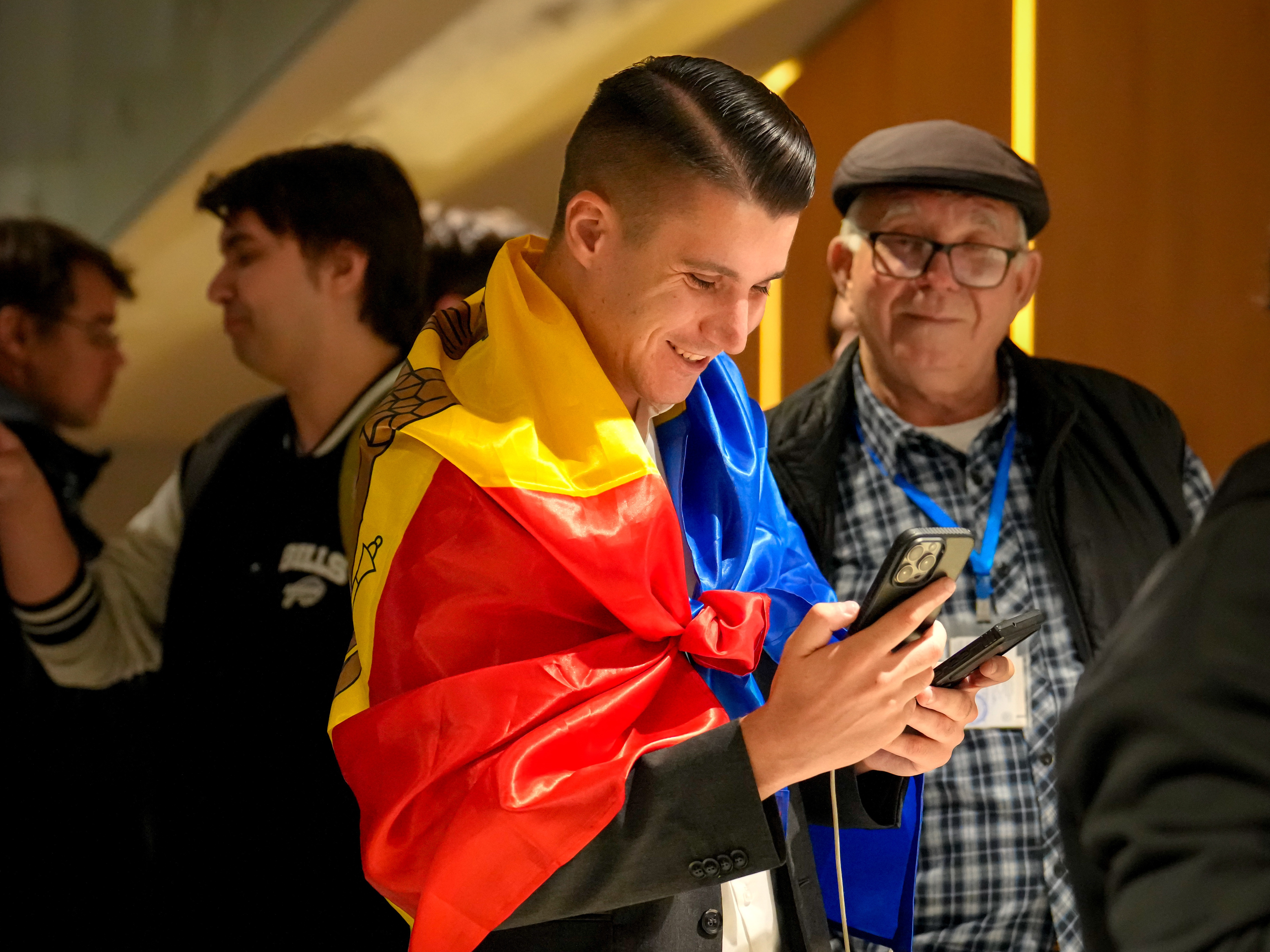 caption: A supporter of the pro-EU Party of Action and Solidarity (PAS) draped in the Moldovan flag smiles as he checks partial results on a phone after the polls closed for the parliamentary election, in Chisinau, Moldova, Sunday, Sept. 28, 2025.