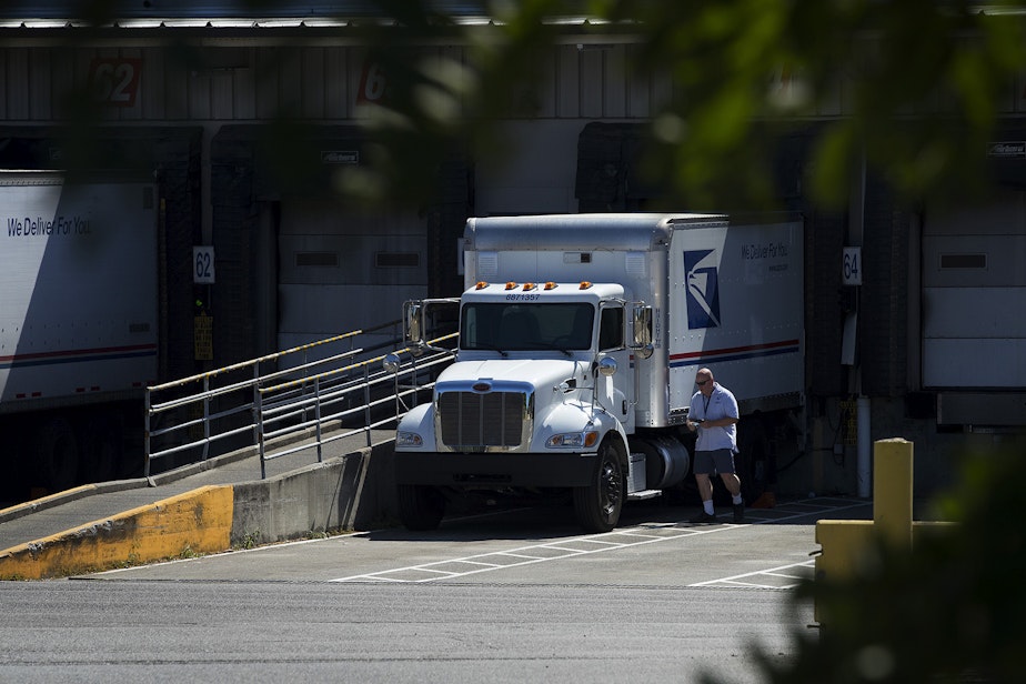 caption: A US Postal Service employee approaches a delivery truck on Aug. 17, 2020, at the Seattle area's main mail-processing center on 27th Avenue South in Tukwila. 