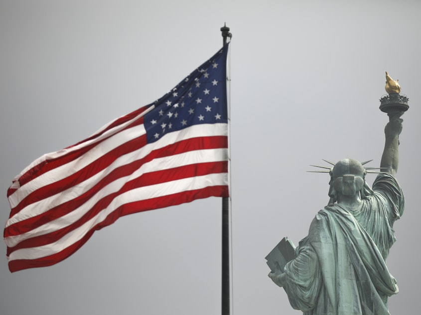 caption: An America flag flies near the Statue of Liberty on Liberty Island.