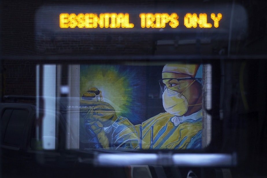caption: A mural of a health care worker painted by artist Jay Mason is shown through the window of a passing King County Metro bus on Tuesday, April 28, 2020, along South Main Street in Seattle.