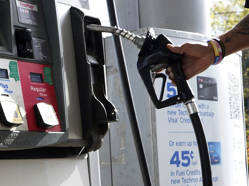 caption: A customer replaces the pump dispenser at a Chevron gas station in Columbus, Miss., on Oct. 23. The average price of regular gas has fallen more than 40 cents from a year ago.