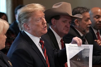 caption: President Trump holds a picture labeled "typical standard wall design" as he hosts a roundtable discussion on border security in the Cabinet Room of the White House on Friday.