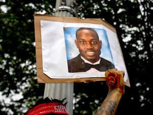 caption: A person protesting racial injustice holds a photo of Ahmaud Arbery during a May 2020 march in Washington, D.C.