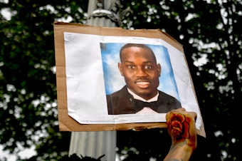caption: A person protesting racial injustice holds a photo of Ahmaud Arbery during a May 2020 march in Washington, D.C.