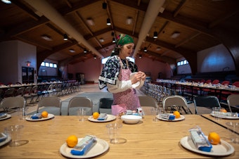 caption: Cloe McMichael, 22, sets the table in the longhouse in Mission, Oregon, ahead of the annual Indian New Year ceremony, which is celebrated on the Winter Solstice. The feast is a celebration of the Confederated Tribes of the Umatilla Indian Reservation’s sacred first foods and their renewal each year. Each place setting includes a set of reusable utensils, provided by the CTUIR Department of Natural Resources.