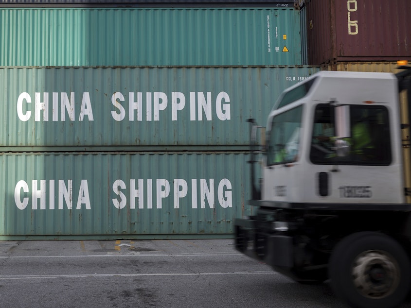 caption: A truck passes a stack of China Shipping containers at the Port of Savannah in Georgia on July 5, 2018. The Trump administration is delaying some tariffs from taking effect until December.