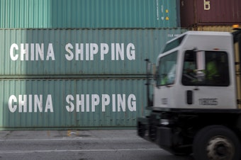 caption: A truck passes a stack of China Shipping containers at the Port of Savannah in Georgia on July 5, 2018. The Trump administration is delaying some tariffs from taking effect until December.