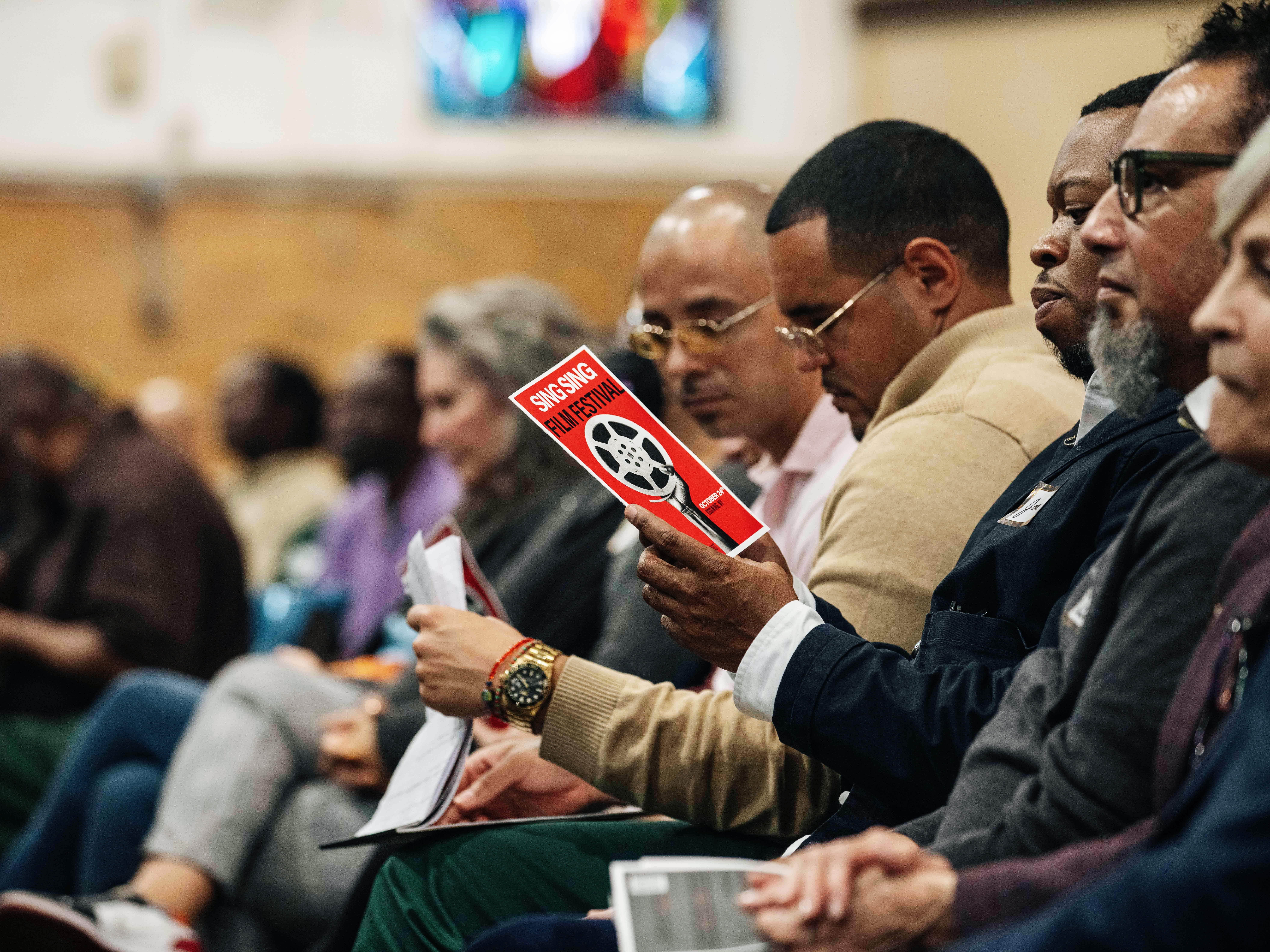caption: Guests and incarcerated men sit alongside each other at the Sing Sing Correctional Facility's first-ever film festival on Oct. 24.