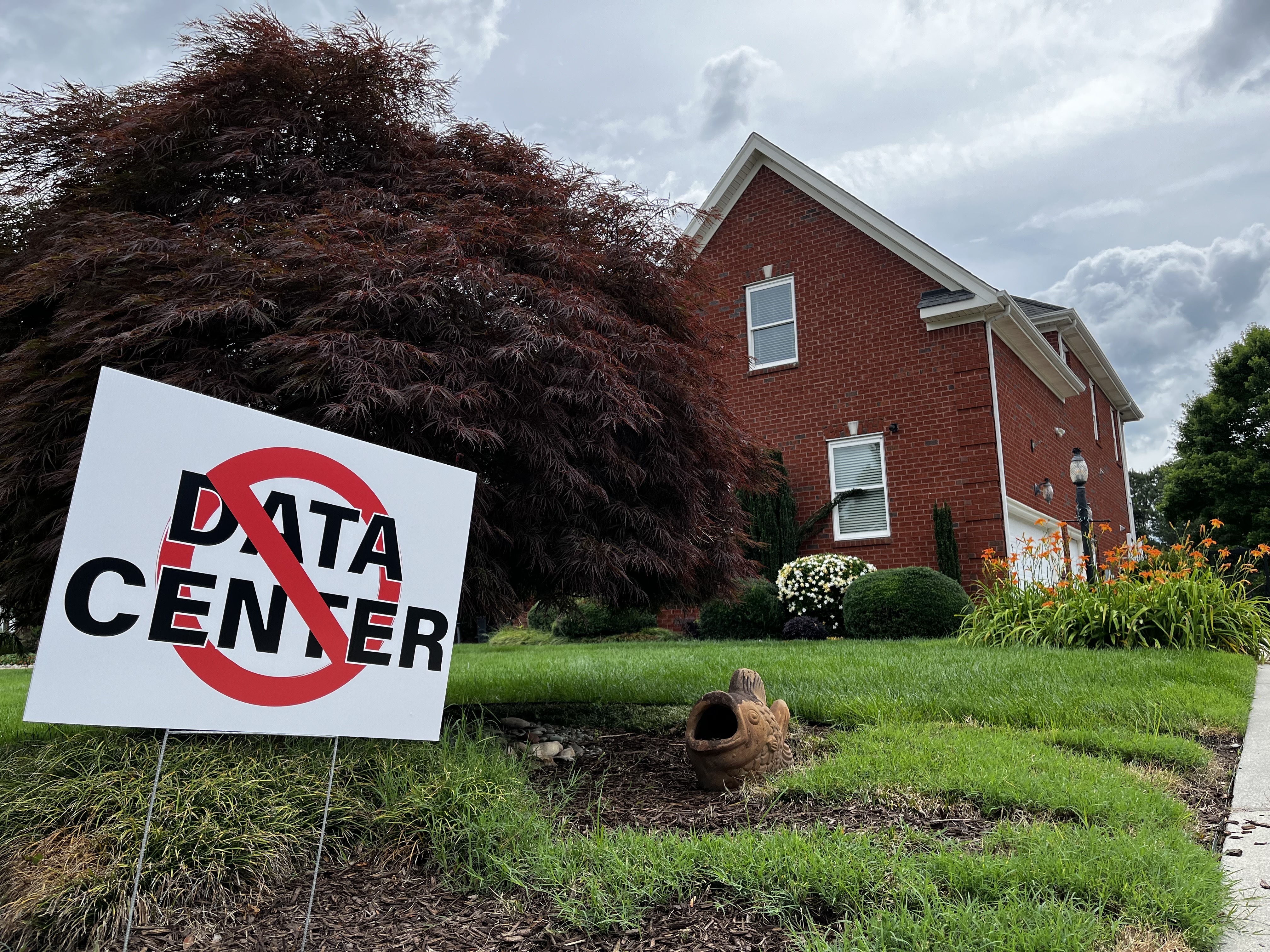 caption: The yard of a house in Chesapeake, Va., displays a sign opposing the construction of data centers.