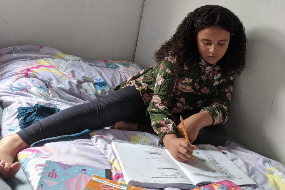 caption: Eight-year-old Mariana Aceves does her homework on her bed inside a tiny home. 
