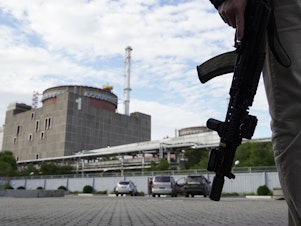 caption: A security person stands in front of the Zaporizhzhia nuclear power plant on September 11.