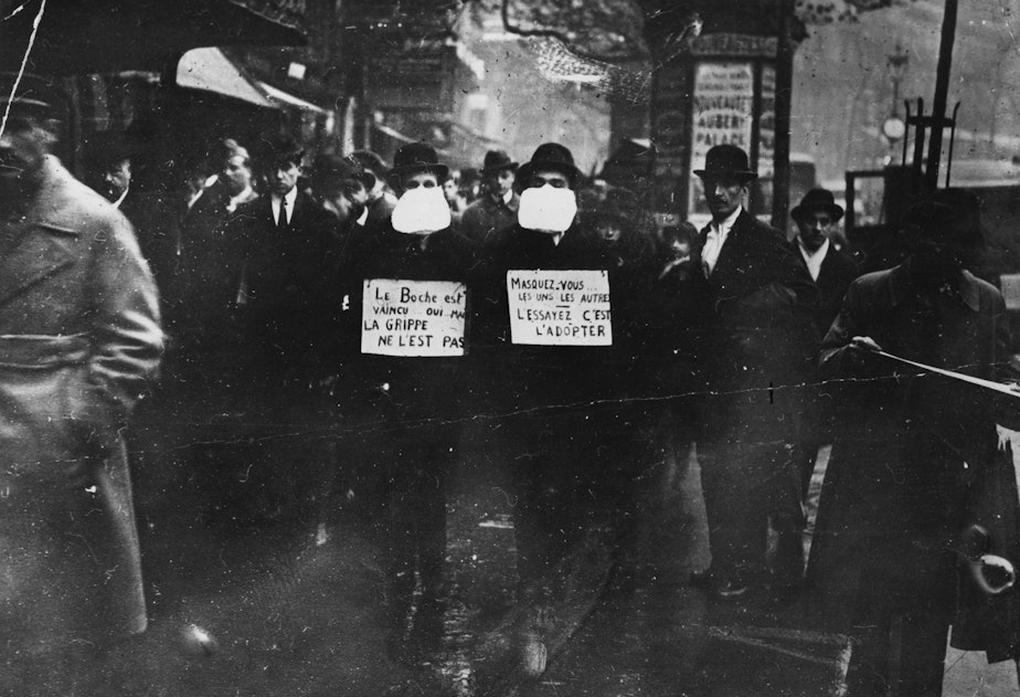 caption: Two men wearing and advocating the use of flu masks in Paris during the Spanish flu epidemic which followed World War I.  (Topical Press Agency/Getty Images)