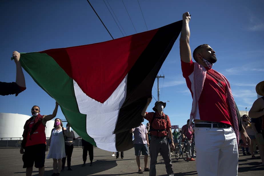 caption: Activists and allies of the Palestinian feminist organization Falastiniyat, including Omar Elseaidy, right, carry the flag of Palestine while blocking an intersection in protest of the ZIM San Diego vessel, on Thursday, June 17, 2021, at the Port of Seattle. "We are now calling on our city officials to stand behind their communities against Israeli human rights abuses, and not to give into the bullying of the apartheid state of Israel," said Aisha Mansour, a representative of Falastiniyat. 