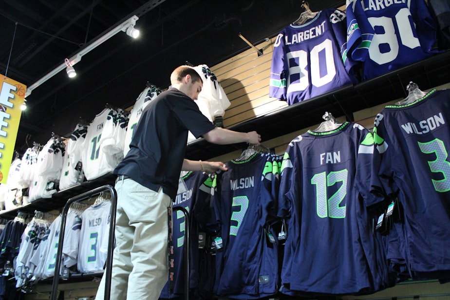 caption: Tom McMaster, of Just Sports in Alderwood Mall, hangs more "12th Man" uniforms. The success of the team has made them hot commodities.
