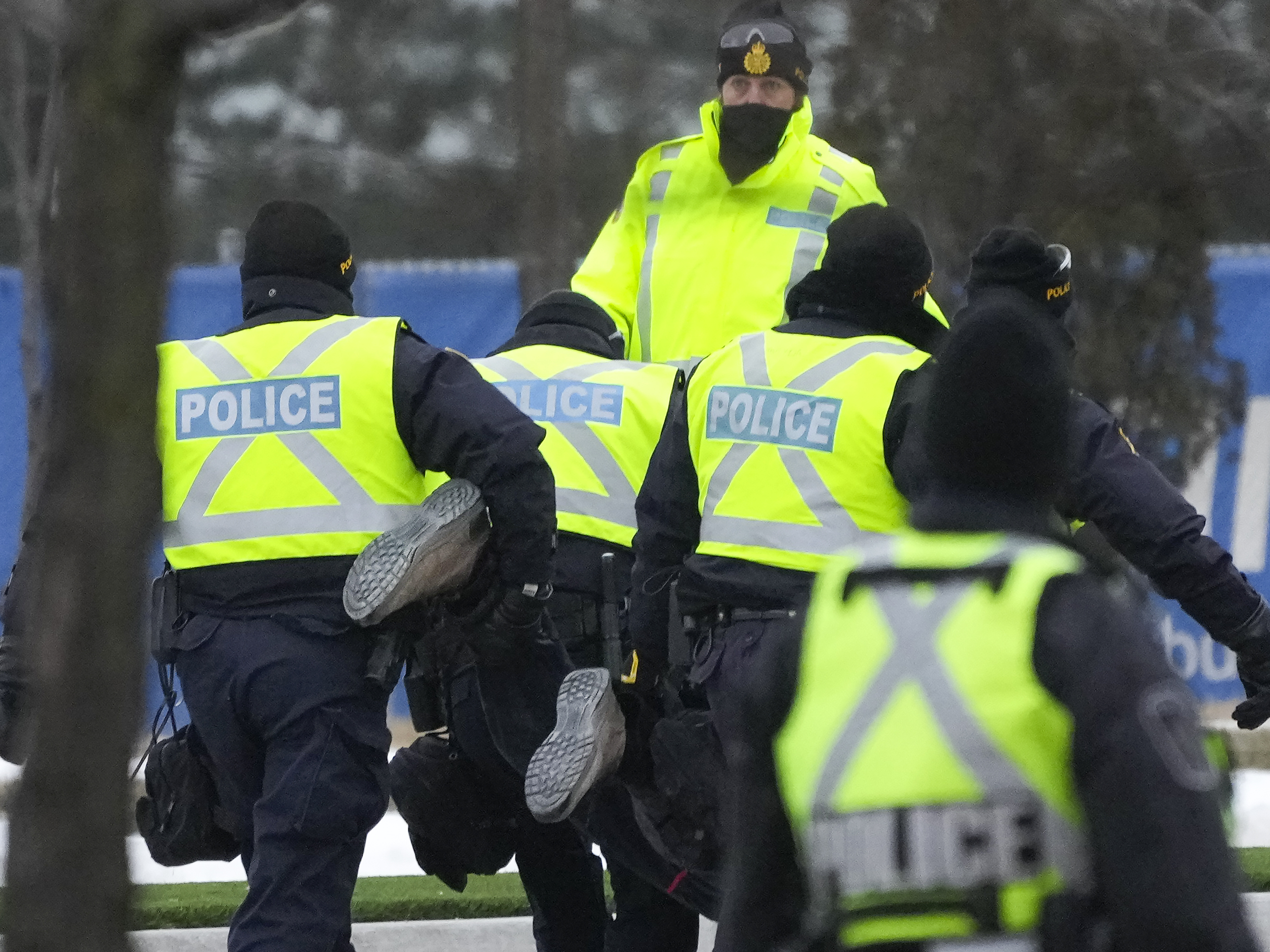 caption: Police arrest a person as they walk the line to remove all truckers and supporters after a court injunction gave police the power to enforce the law after protesters blocked the access leading from the Ambassador Bridge, linking Detroit and Windsor, as truckers and their supporters continue to protest against COVID-19 vaccine mandates and restrictions in Windsor, Ontario, Sunday.