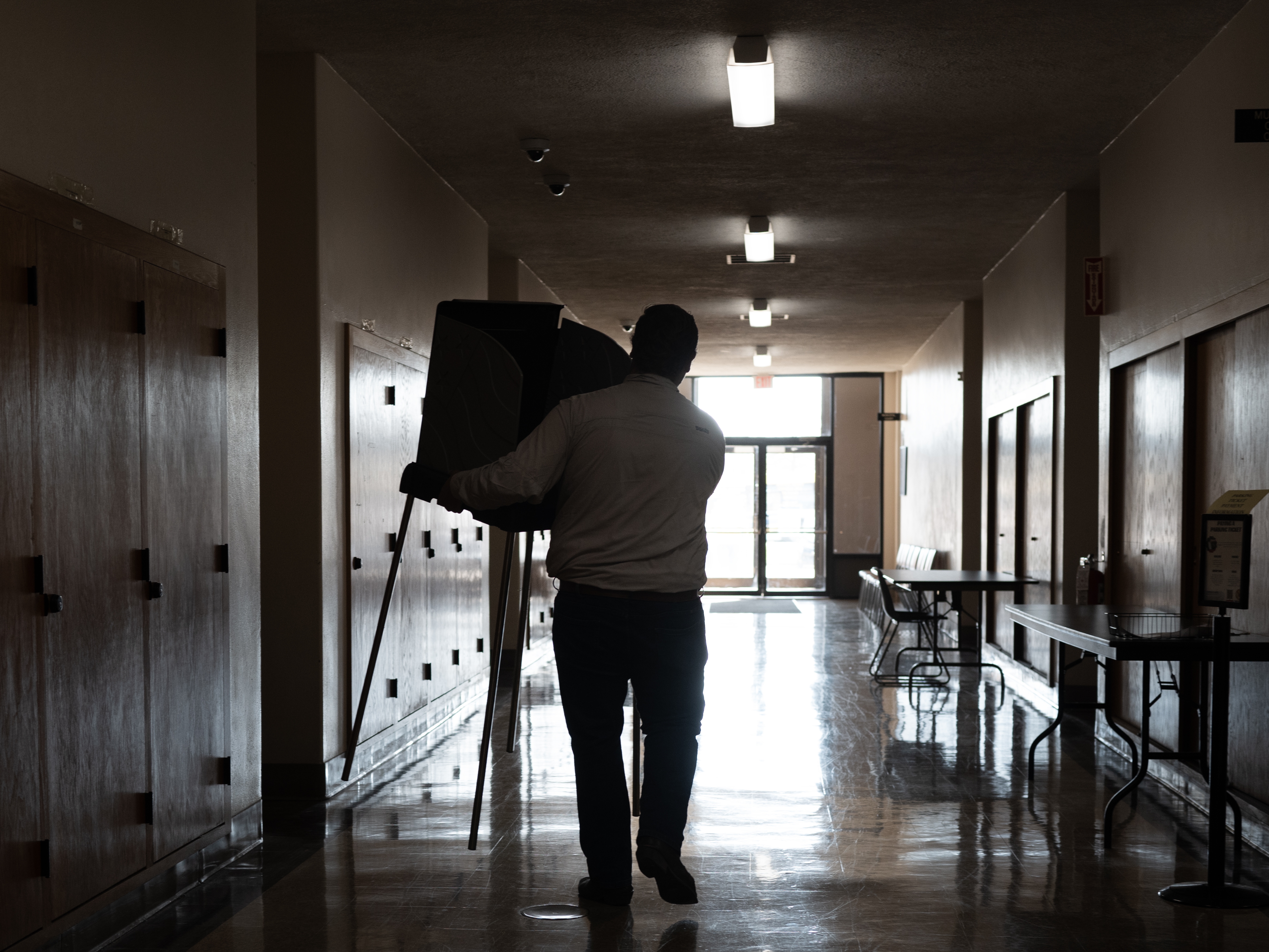 caption: A staffer with the Kenosha County clerk's office sets up voting booths on Oct. 21, 2024, in preparation for in-person early voting in Kenosha, Wis.