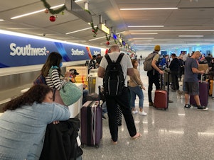 caption: Travelers wait at a Southwest Airlines baggage counter after flight cancellations hit Los Angeles International Airport on Monday. The airline warns it will fly about one-third of its schedule for the next several days.