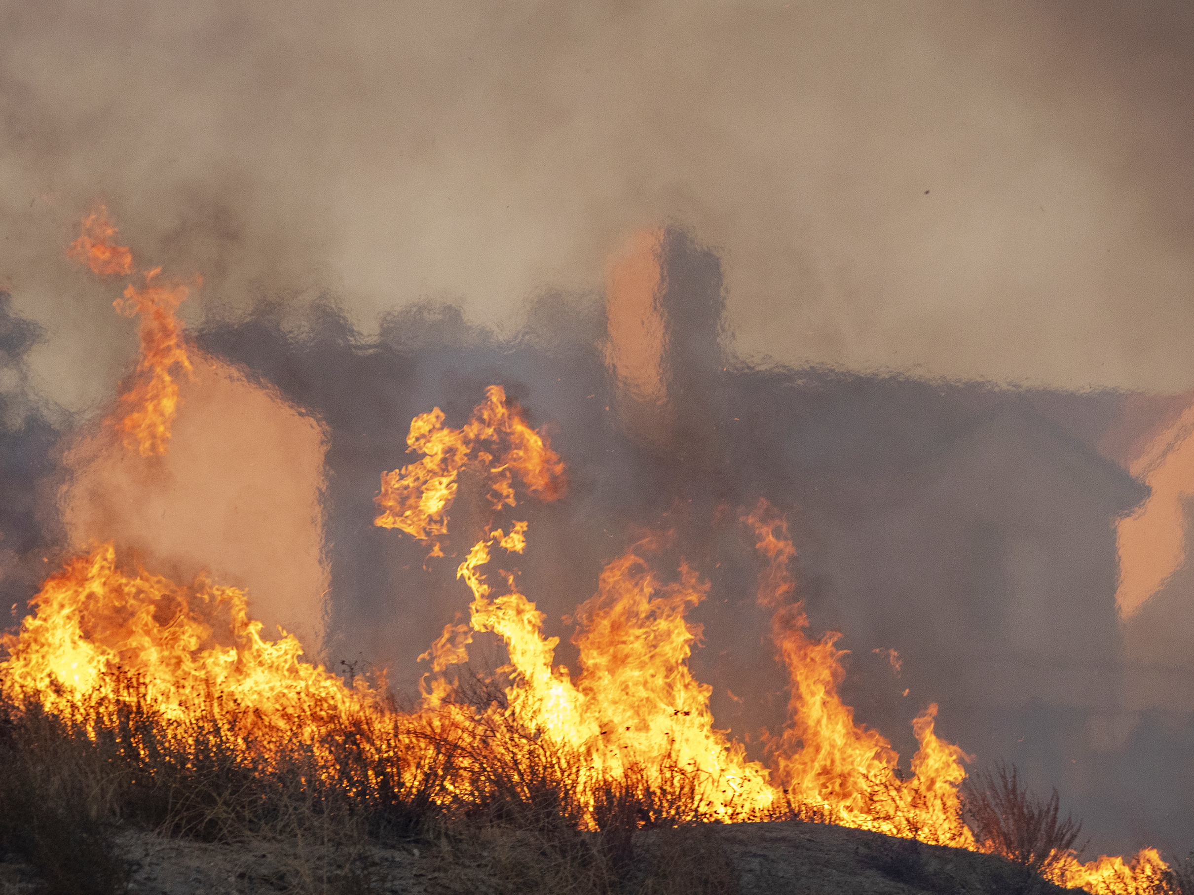 caption: Flames approach houses during the Tick Fire on Oct. 24, 2019 in Canyon Country, California.