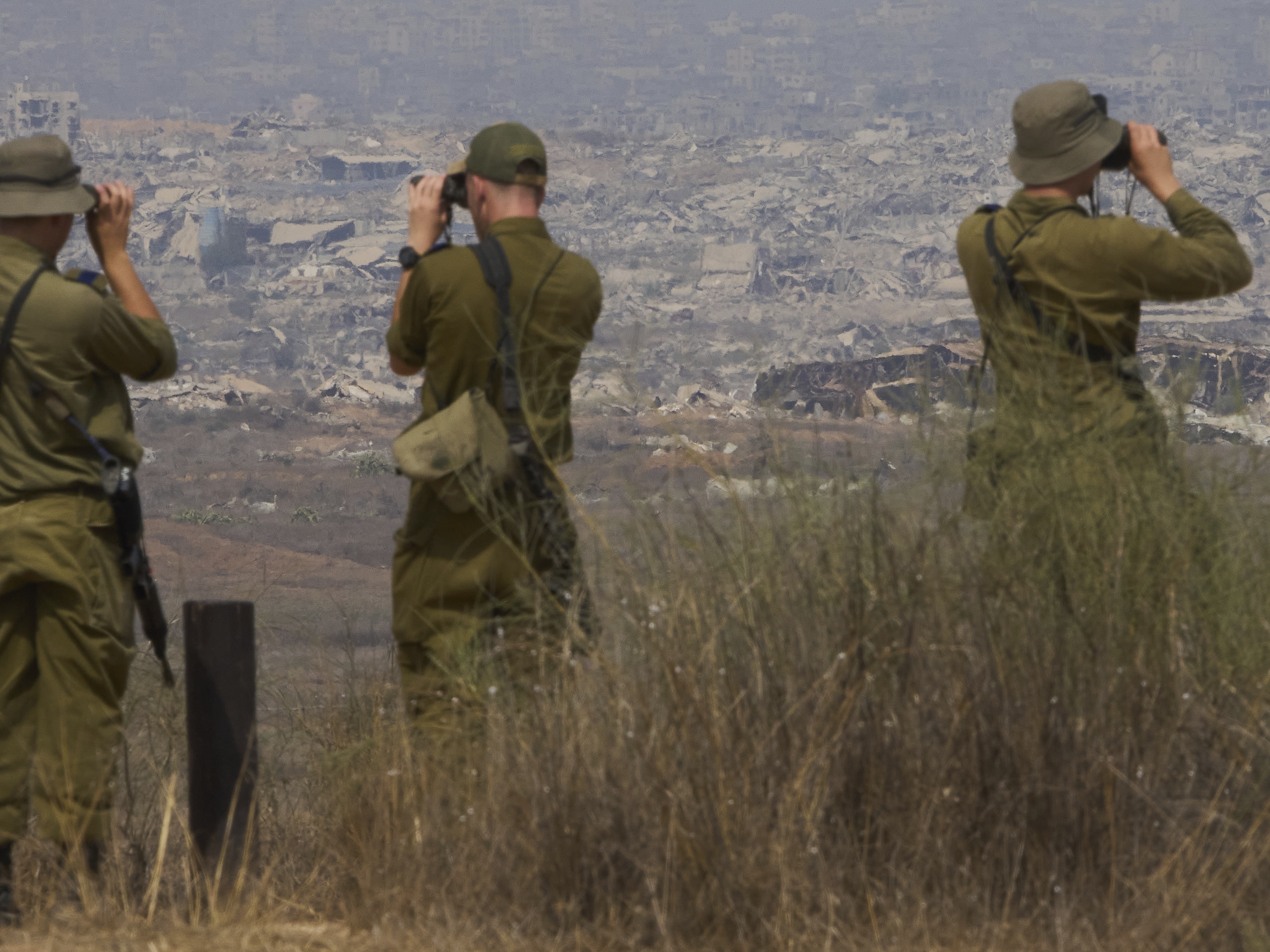 caption: Israeli soldiers uses binoculars to look at damaged buildings in the Gaza Strip, from southern Israel, Wednesday, Aug. 13, 2025.