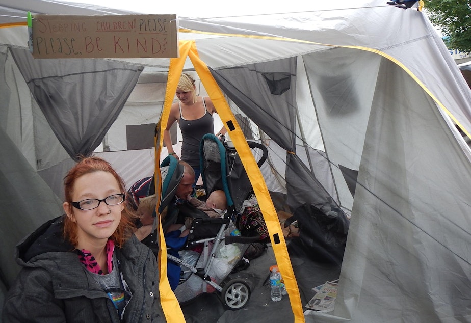 caption: Jackie O'Bryan in front of her family's tent at a University District homeless camp earlier this year.