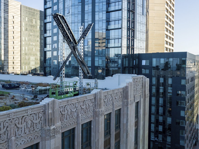 caption: An "X" sign rests atop the company headquarters in downtown San Francisco, on July 28, 2023.