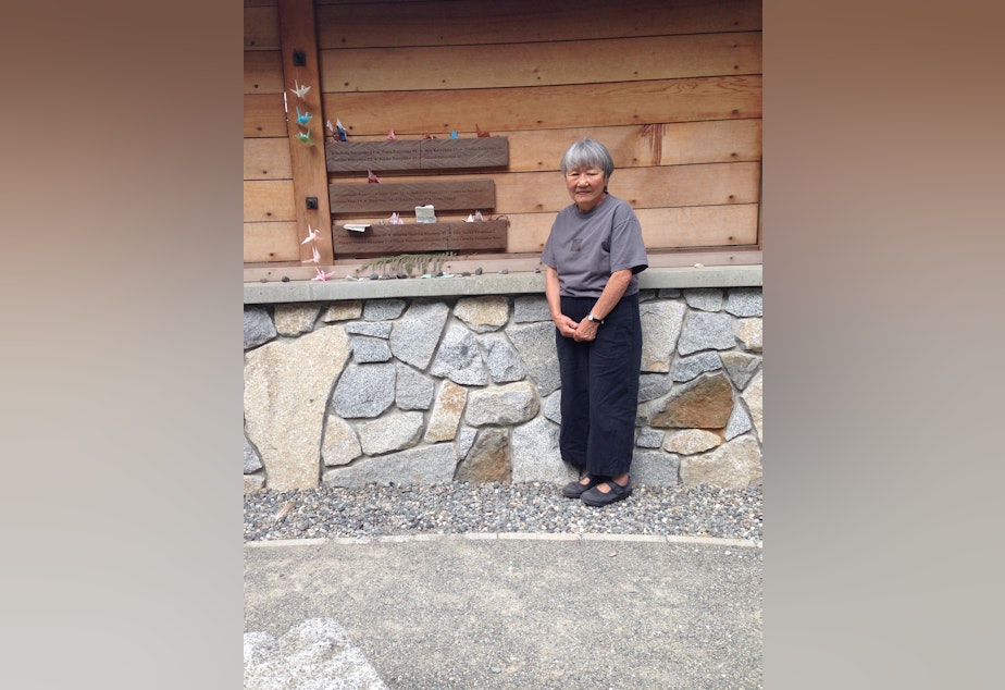 caption: Lily Kodoma stands in front of the Bainbridge Island Japanese American Exclusion Memorial. Kodoma's name, along with her parents and brothers and sisters, are inscribed on the wall behind her. 