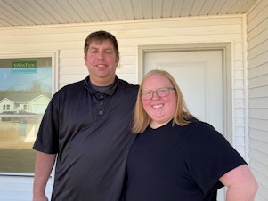 caption: Cook employees Ryan and Shelby Bixler stand in front of the house they're buying from the company. They say they never could have afforded a new place like this at the full market price.