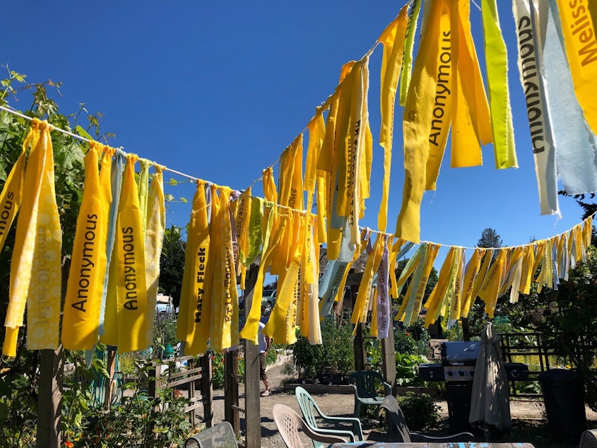 caption: Yellow flags over the garden's empty community dining area bear the names of donors who've funded the garden's effort to save itself from development.