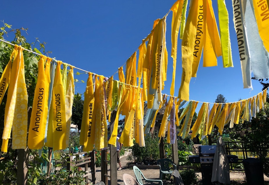 caption: Yellow flags over the garden's empty community dining area bear the names of donors who've funded the garden's effort to save itself from development.