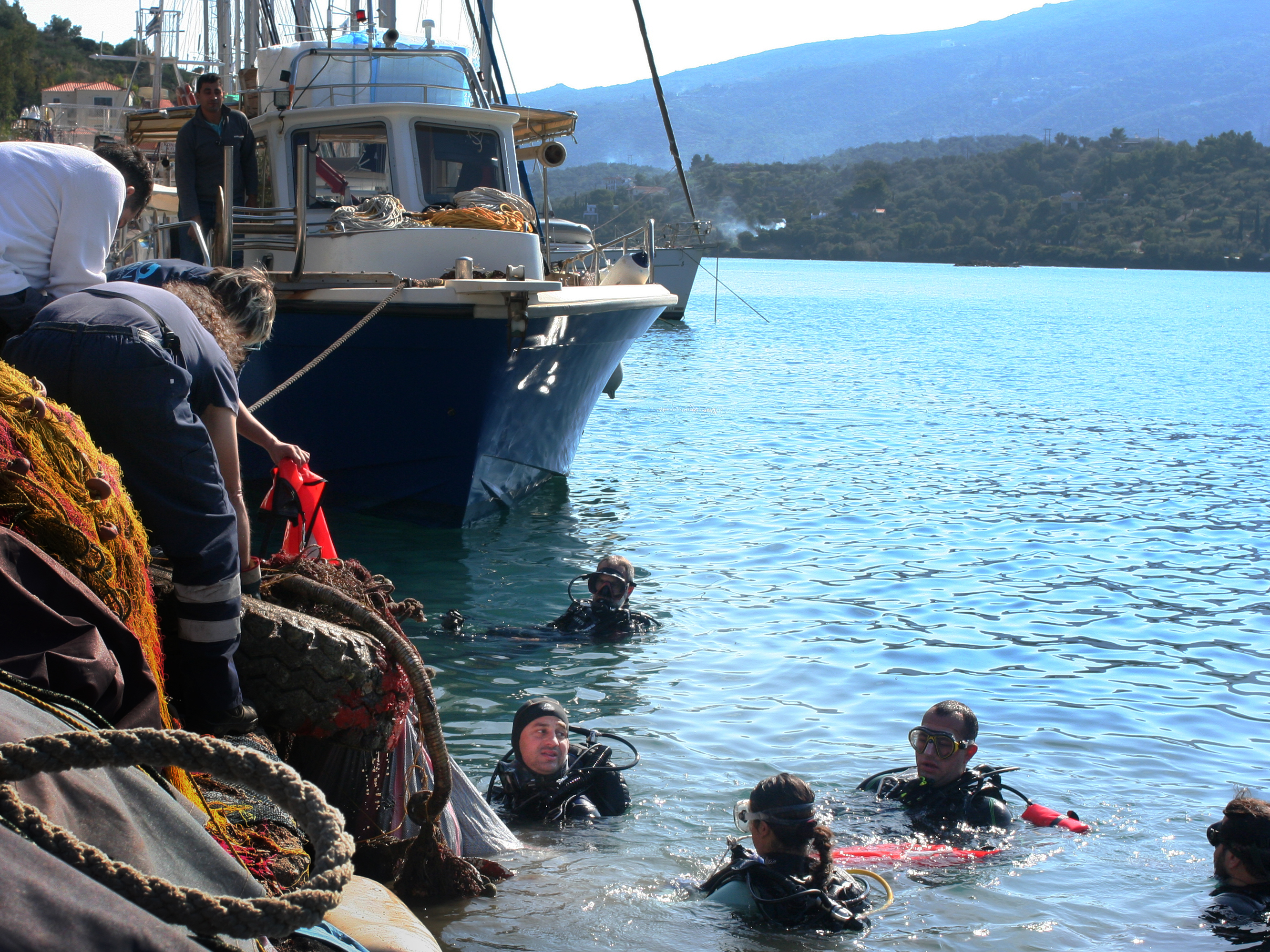 caption: Aegean Rebreath founder George Sarelakos (center) hands a netted bag of marine litter to volunteers on the main pier of the Greek island of Poros.