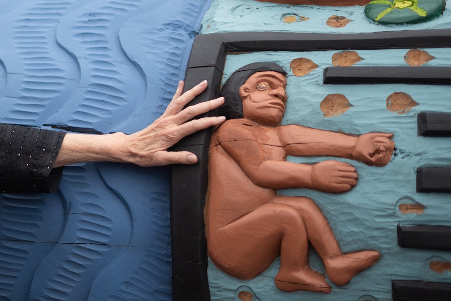caption: A woman’s hand touches the 24-foot totem pole after an invitation by the carvers to do so, on Saturday, May 22, 2021, outside of Seattle's Pike Place Market. 