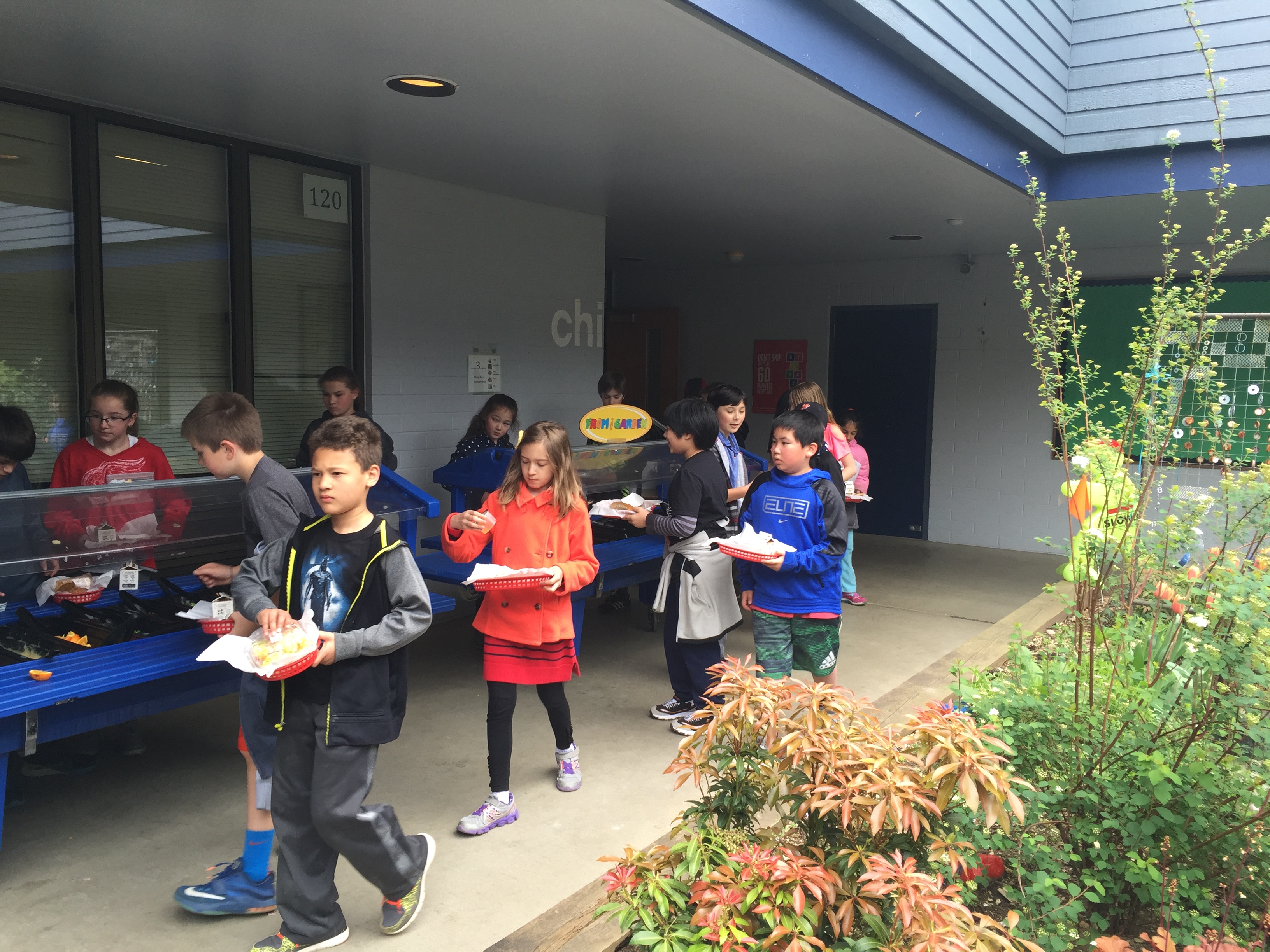 caption: Students at Margaret Mead Elementary in Sammamish load their lunch trays beneath a canopy of bird netting. The school is so crowded that children line up for lunch outside.