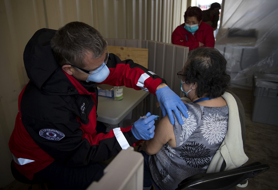 caption: Seattle Firefighter and EMT Garth Stroyan, left, administers the first dose of the Moderna Covid-19 vaccine for Mayra Murtha, right, on Thursday, February 18, 2021, at the West Seattle Covid-19 testing site on Southwest Thistle Street in Seattle. A pop-up vaccination clinic was set up for Latinx community members who were referred by El Comite or Villa Comunitaria. 