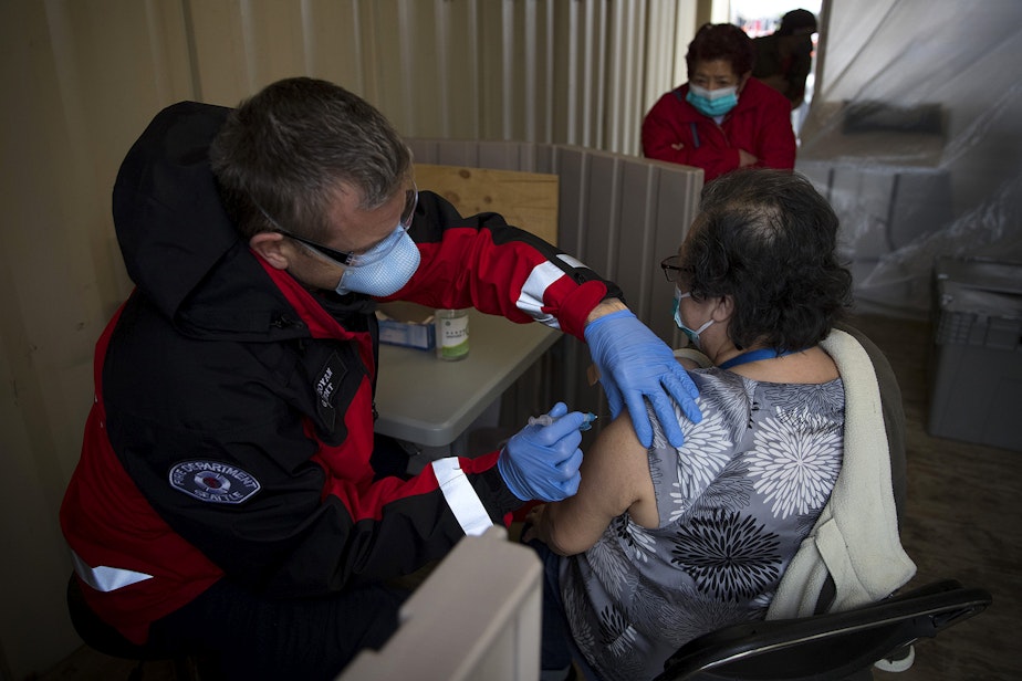 caption: Seattle Firefighter and EMT Garth Stroyan, left, administers the first dose of the Moderna Covid-19 vaccine for Mayra Murtha, right, on Thursday, February 18, 2021, at the West Seattle Covid-19 testing site on Southwest Thistle Street in Seattle. A pop-up vaccination clinic was set up for Latinx community members who were referred by El Comite or Villa Comunitaria. 